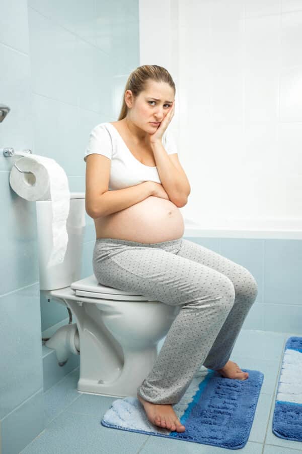 Young pregnant woman sitting on the toilet