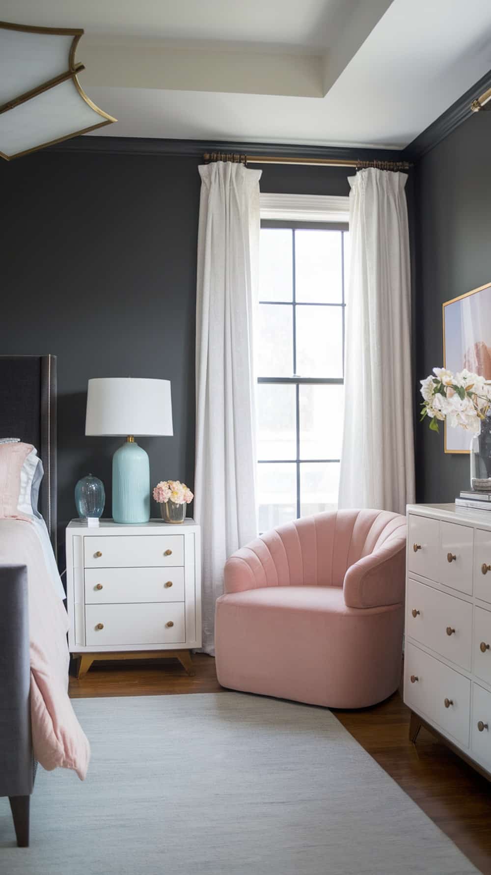 A stylish charcoal gray bedroom featuring soft color accents like a pink chair and light blue lamp.