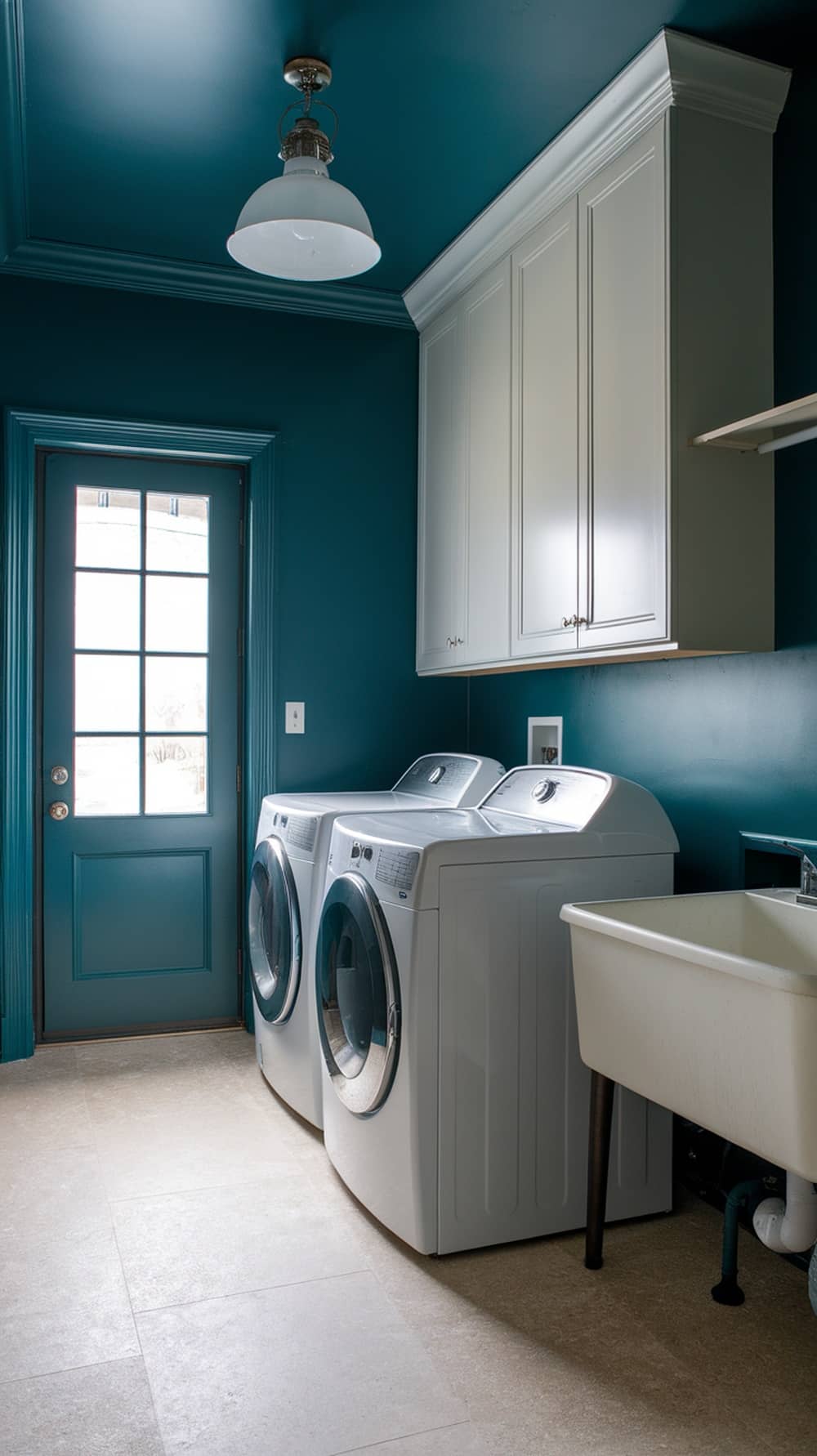 Laundry room with dark teal walls and white trim, featuring modern appliances and a light fixture.
